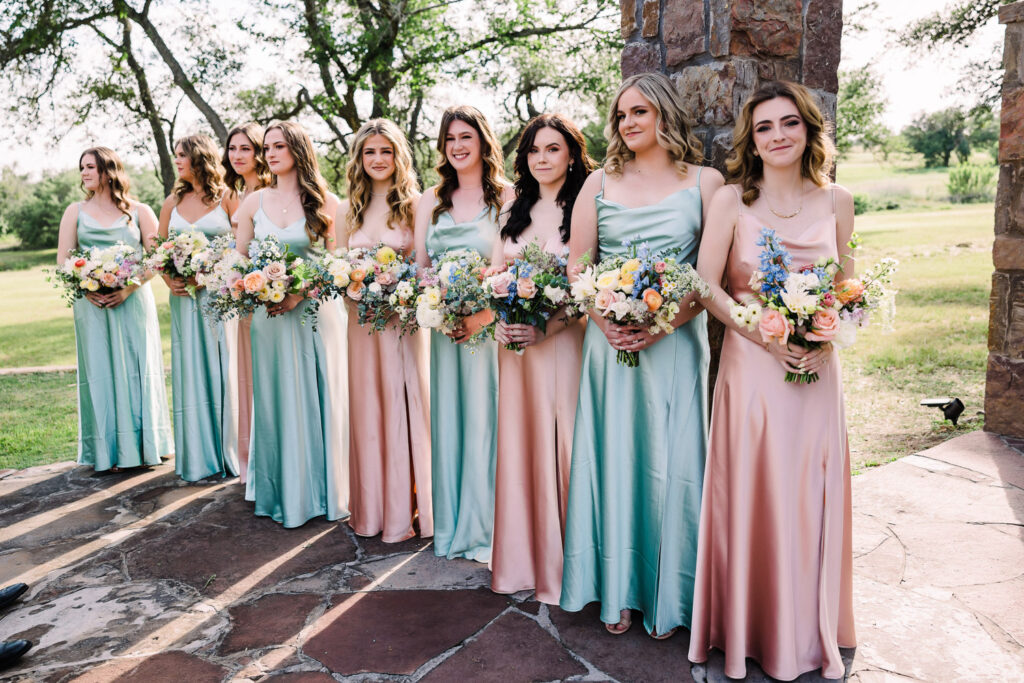 Bridesmaids in pastel satin dresses holding vibrant bouquets at a summer wedding in Austin