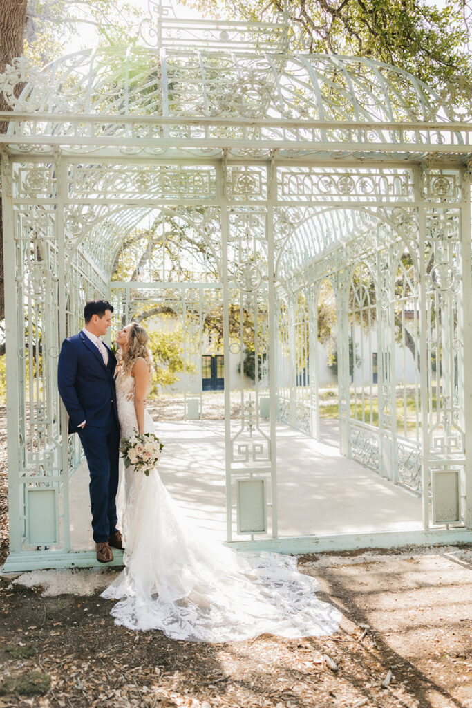 A bride and groom stand beneath a white iron gazebo at Ma Maison highlighting Sustainable Wedding Venues in Austin