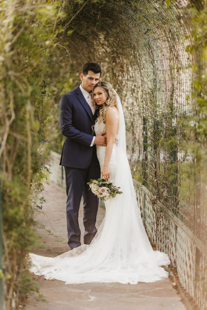 The couple embraces under a green archway surrounded by vines