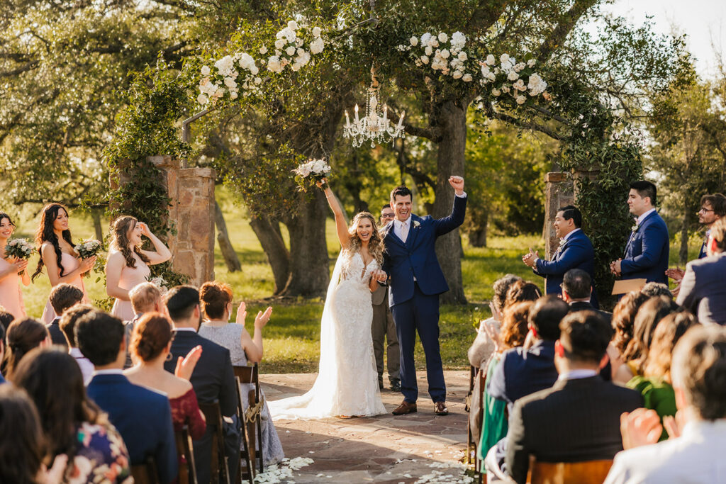 The couple celebrates under a floral arch during their outdoor ceremony