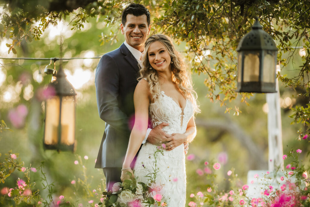 A smiling couple poses together surrounded by garden blooms portraying Sustainable Wedding Venues in Austin