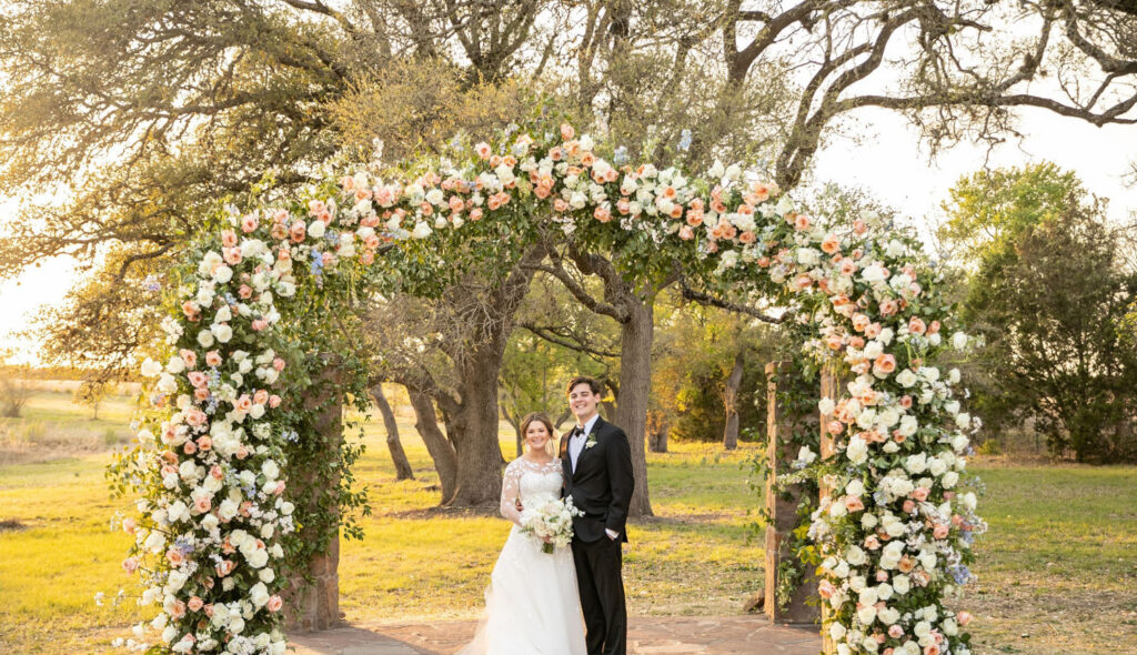 Couple posing under floral arch at sunset