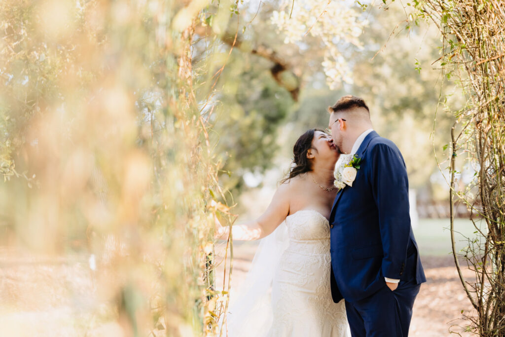 Bride and groom kiss in a sun-drenched garden archway