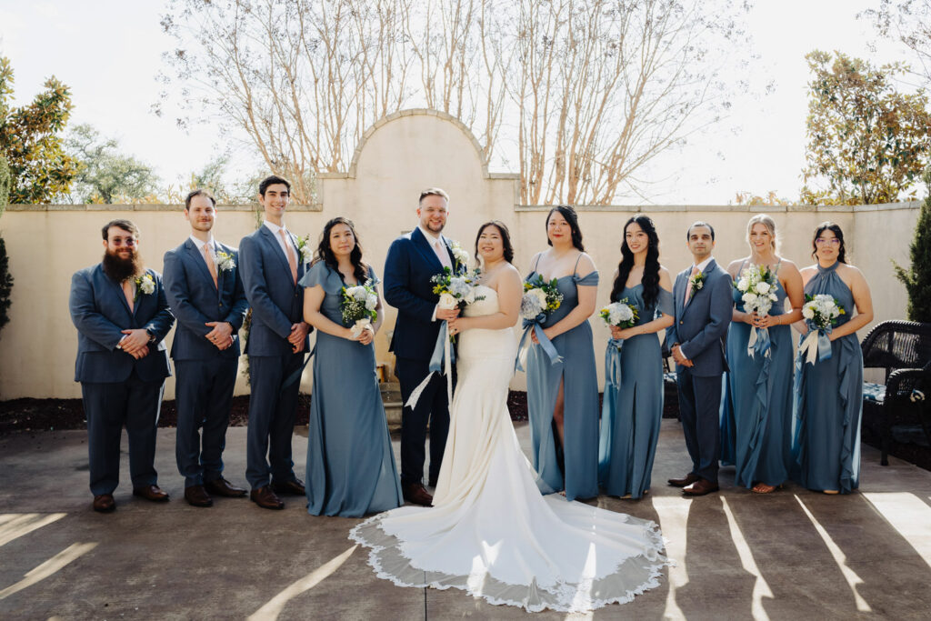Full bridal party dressed in soft blue tones posing with the bride and groom