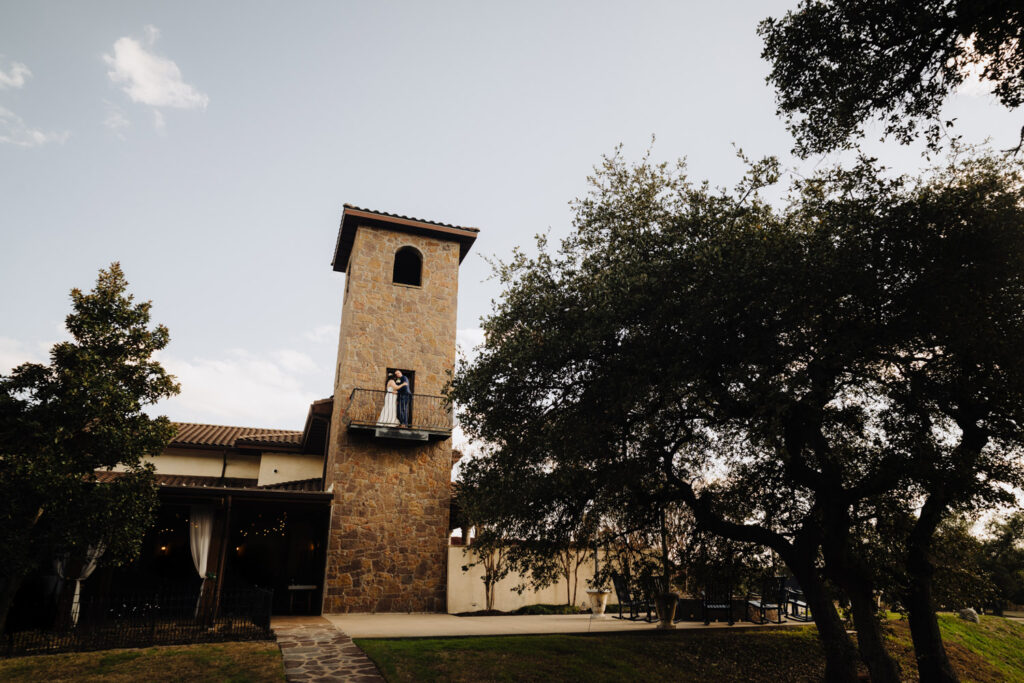 A wide shot of the bride and groom embracing on a stone balcony
