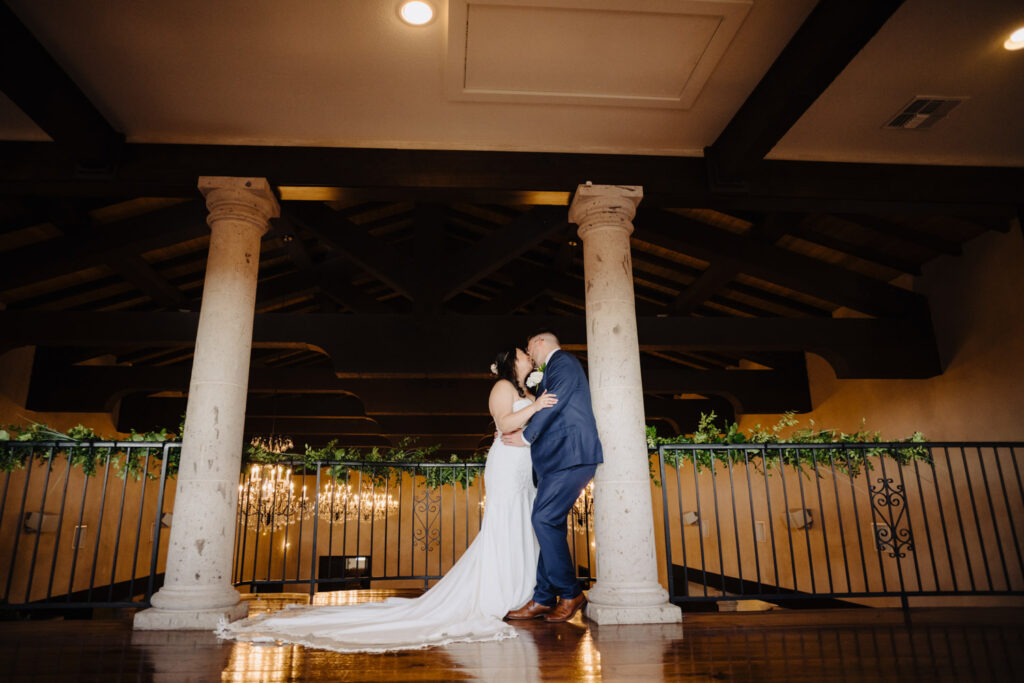 Elegant moment between the bride and groom on an indoor balcony with Tuscan-style pillars and chandeliers
