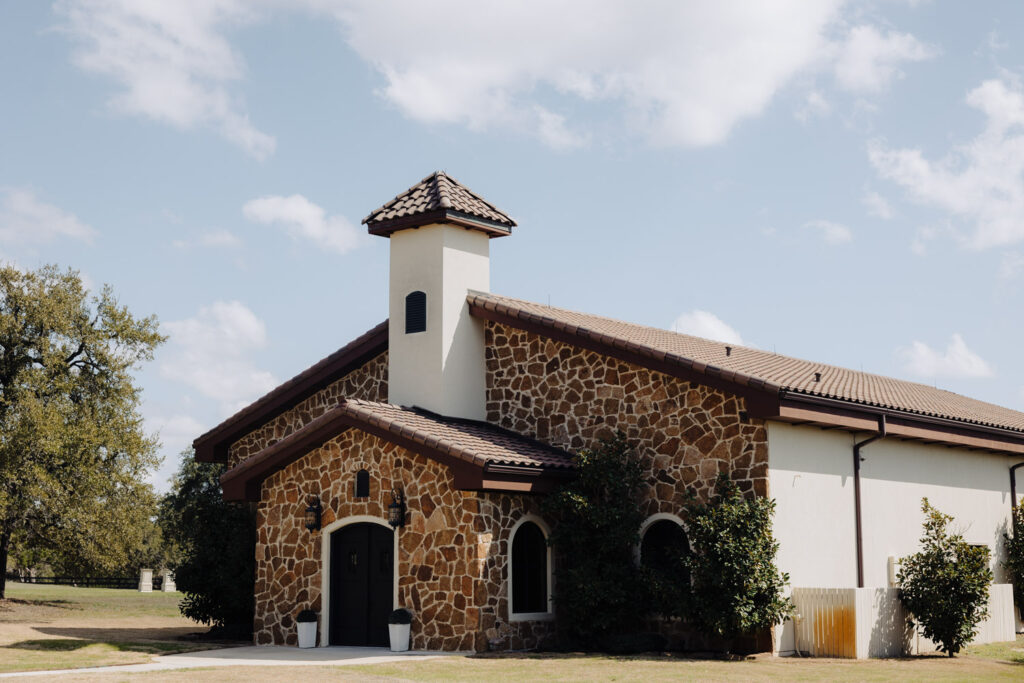 Exterior shot of a stone chapel with Tuscan-style architecture under a clear sky