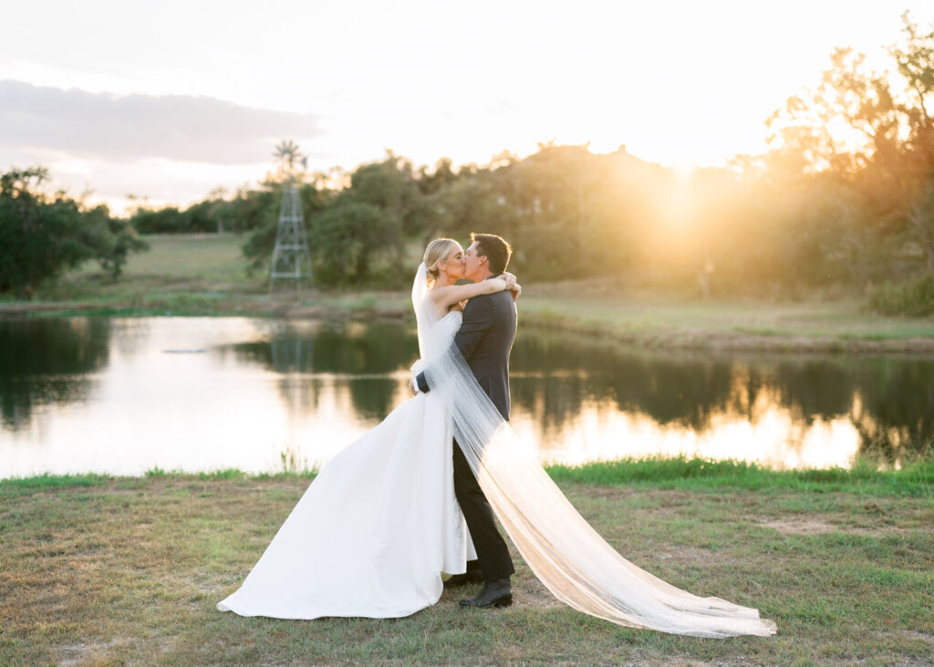 Bride and groom embracing at golden hour near a lakeside backdrop