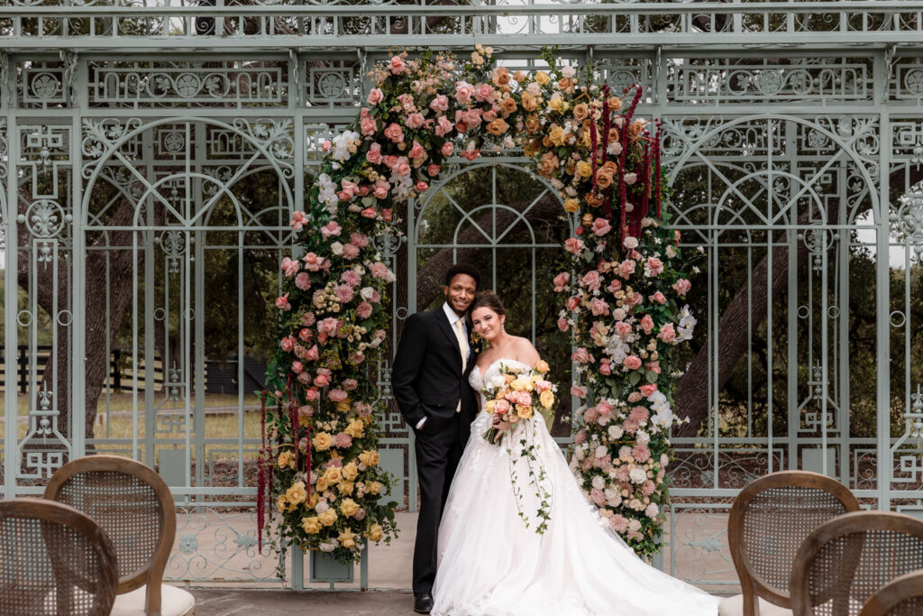 Couple standing beneath a colorful floral arch at Ma Maison
