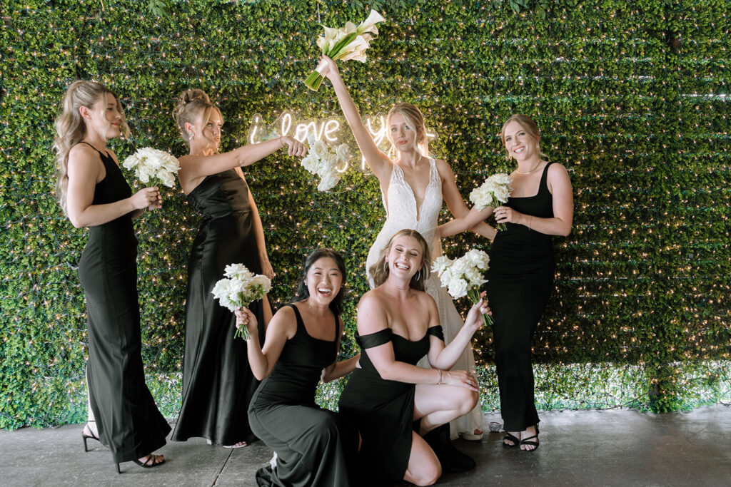 Bride with bridesmaids posing in front of floral backdrop, styled by a Wedding Planner in Austin.