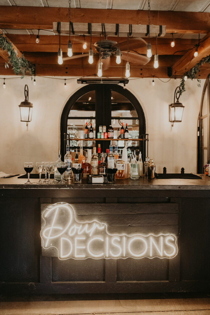 Bar setup with bottles and “Pour Decisions” neon sign