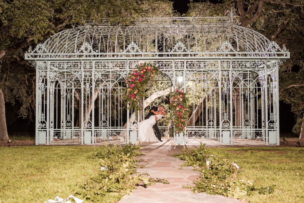 Couple sharing a romantic dip under a floral archway at night during their wedding