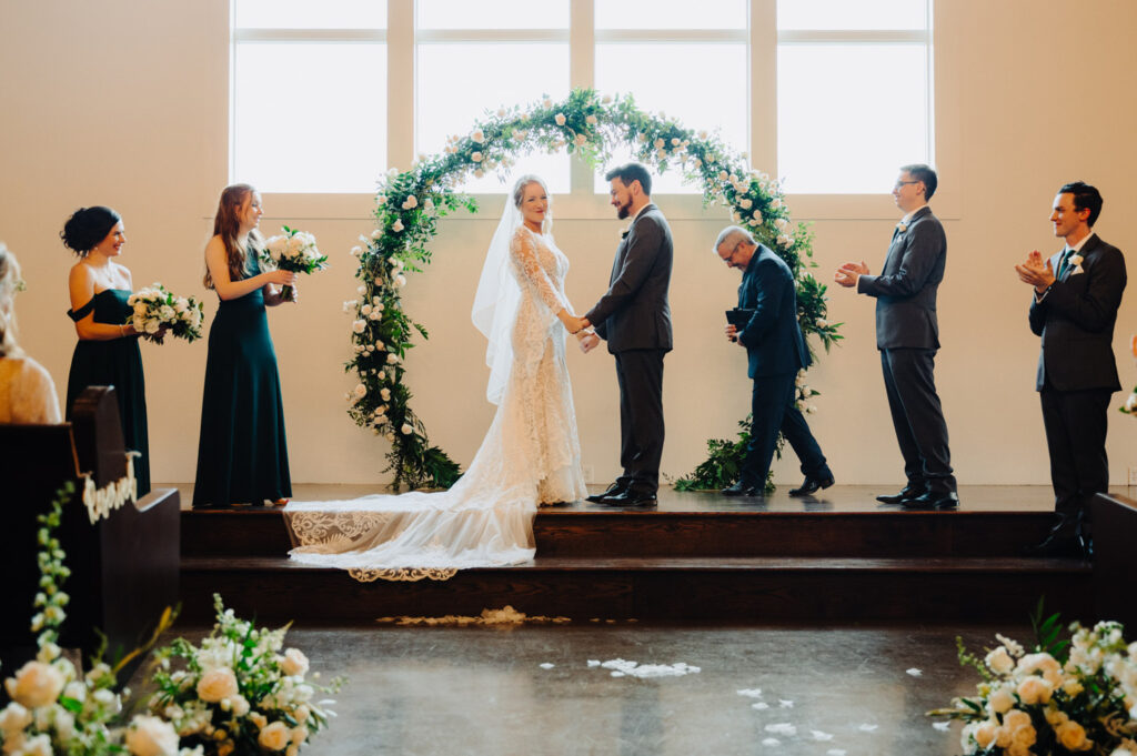 Winter wedding ceremony featuring floral arch and natural light-filled chapel