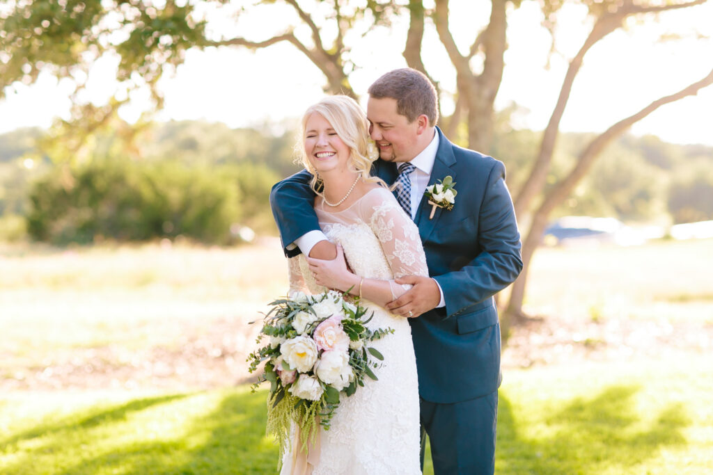 Bride laughing as groom embraces her in the sunshine