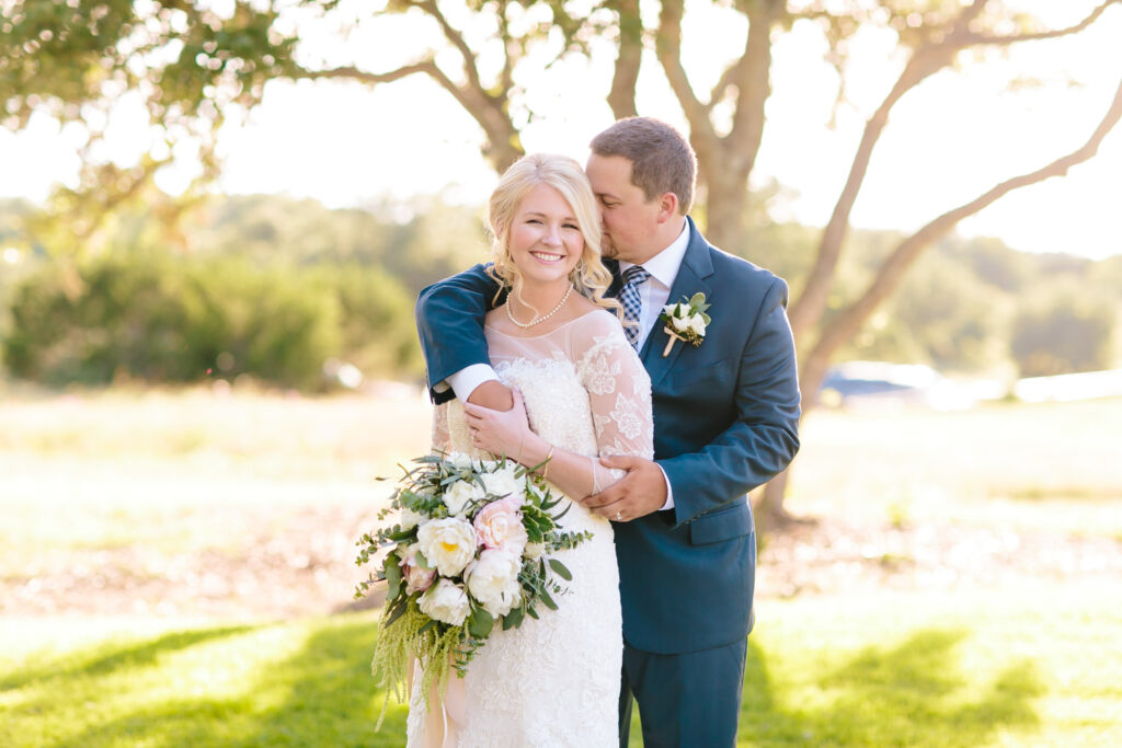 Groom kissing bride’s cheek during golden hour at Ma Maison