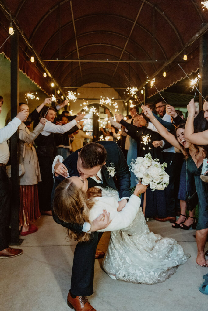 A newlywed couple celebrates their wedding exit at Ma Maison with a sparkler send-off, ending their special day with a romantic dip kiss. Many couples wonder about the average cost of a wedding in Austin, and venues like Ma Maison provide a luxurious yet personalized experience tailored to different budgets.