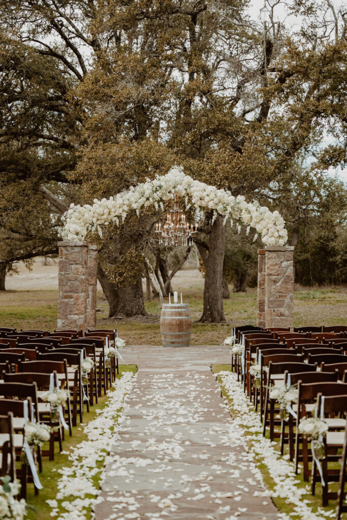 Elegant outdoor wedding ceremony setup under majestic oak trees at Ma Maison, featuring a floral arch and chandelier, ideal for the most popular wedding destination in Austin