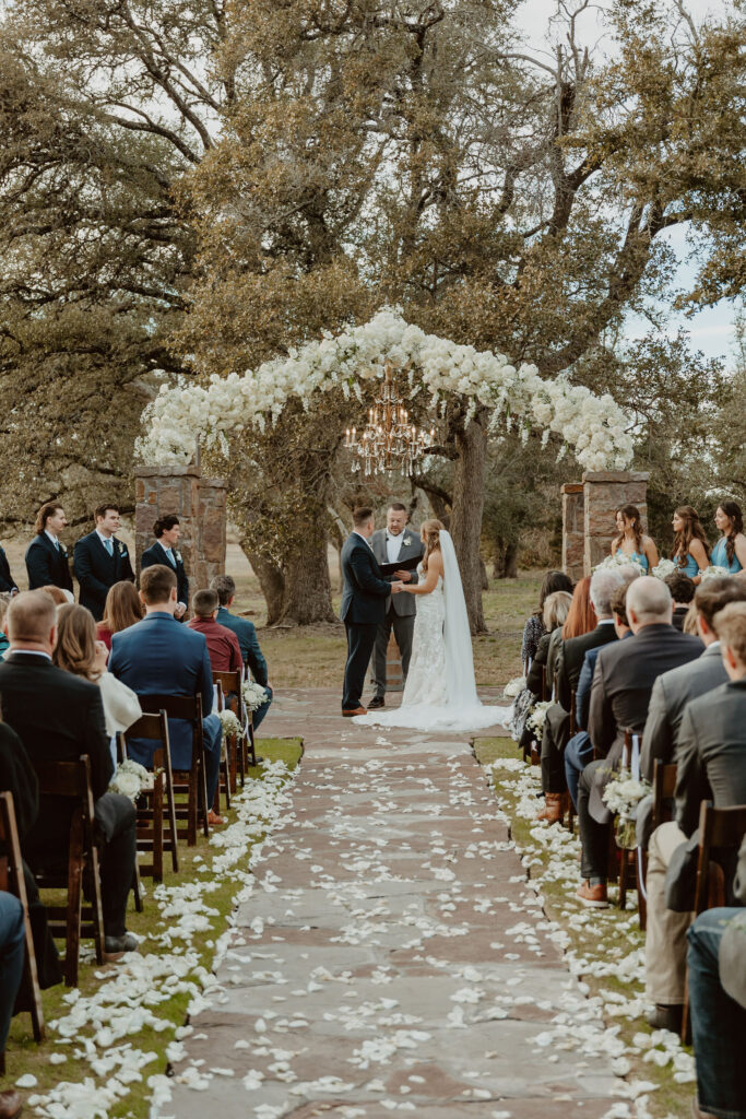 A breathtaking outdoor wedding ceremony at Ma Maison’s Green Cathedral, featuring a floral-adorned tree and a grand chandelier.