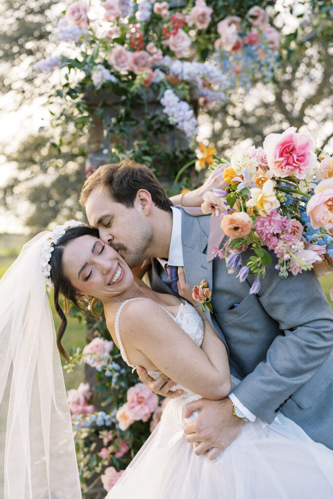 A couple framed by a floral arch of roses, snapdragons, and clematis