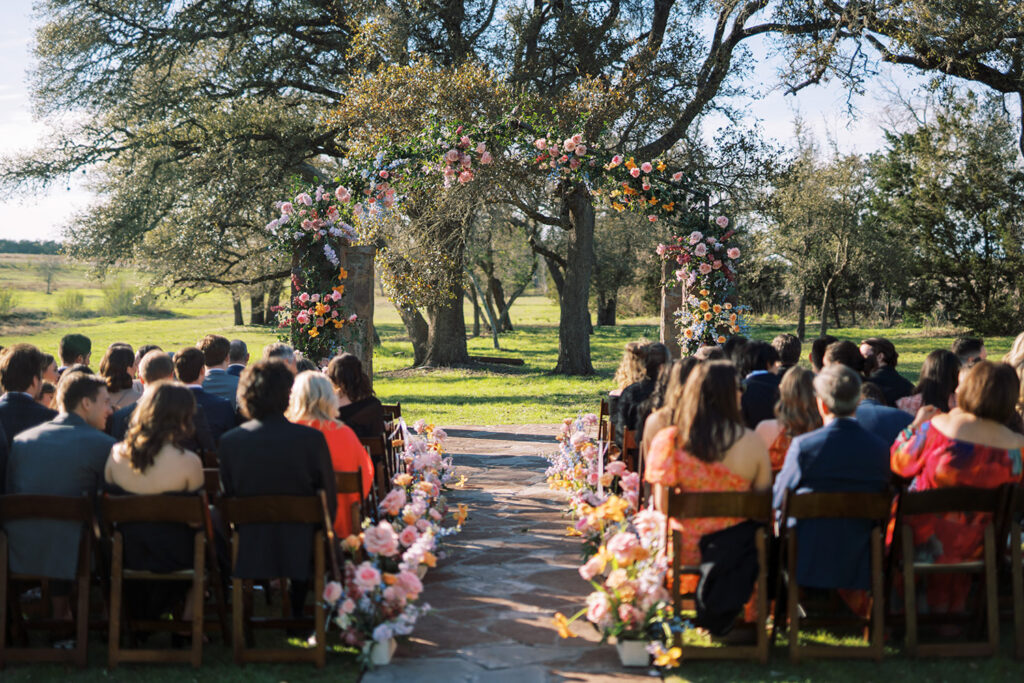 A rustic vase arrangement of orange roses, pink lisianthus, and blue delphiniums perfect for flowers for wedding seating