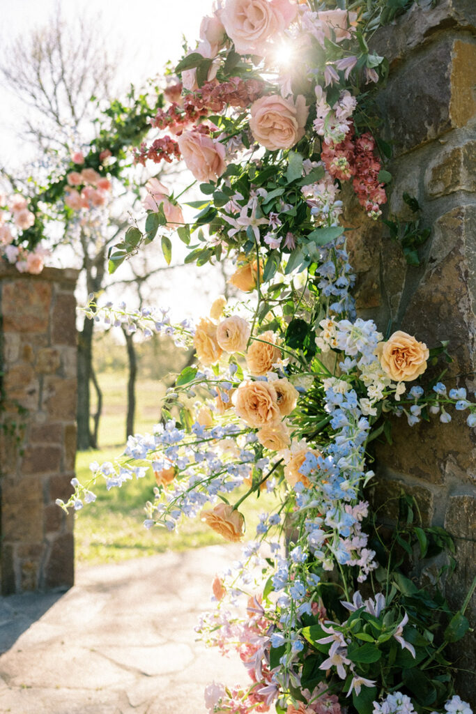 A full altar arch covered in blush roses, lilac stock, and clematis as a stunning example of flowers for wedding backdrops