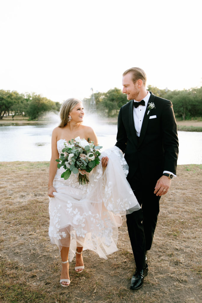 bride and groom walking in front of lake at outdoor Texas wedding venue