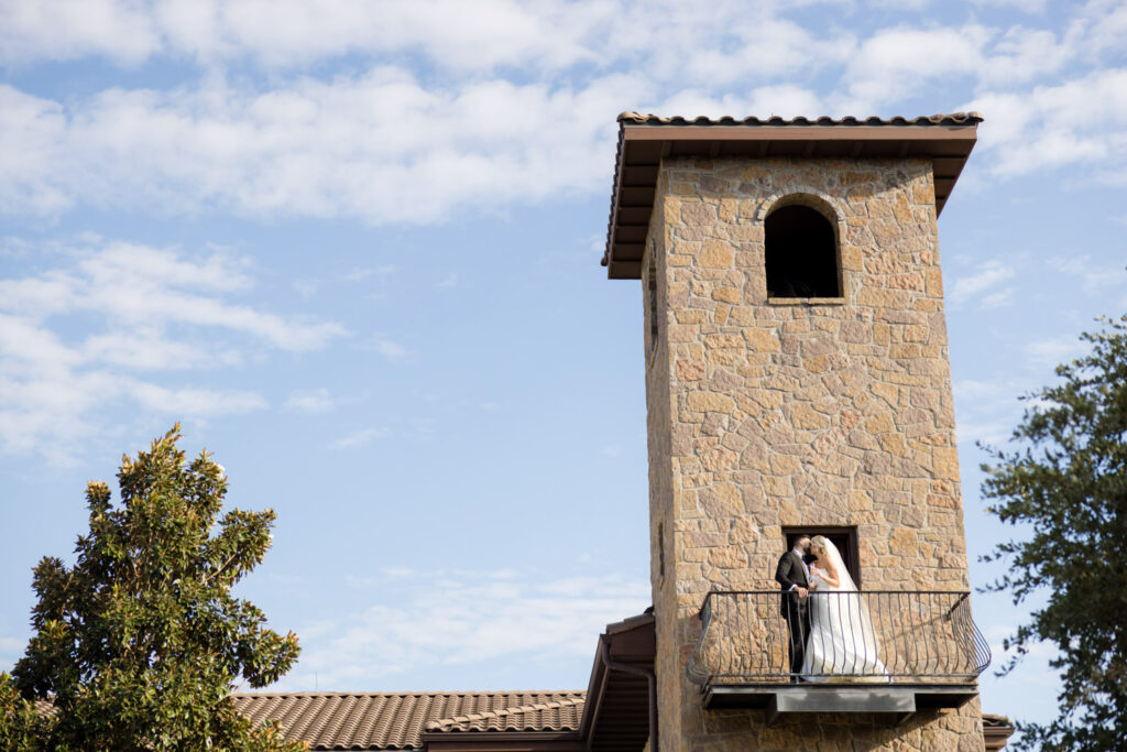 Bride and groom kissing on stone balcony at a romantic Dripping Springs tower