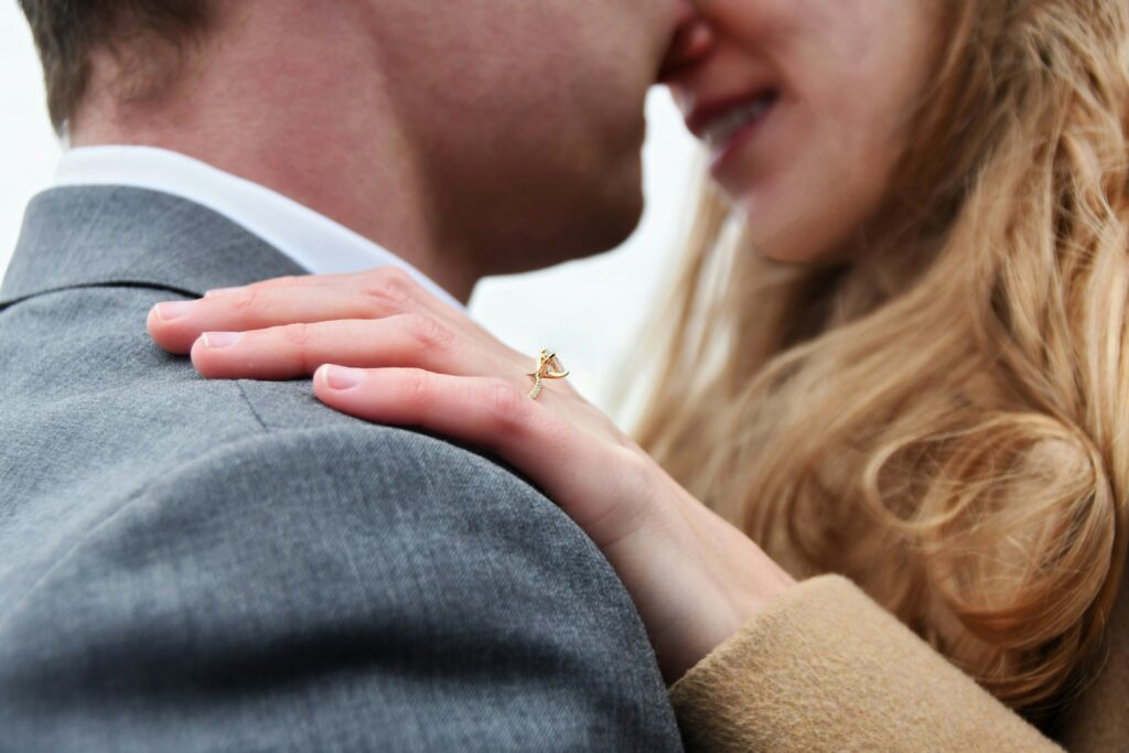 Man and woman about to kiss, while the woman's hand is on the man's shoulder showcasing the engagement ring