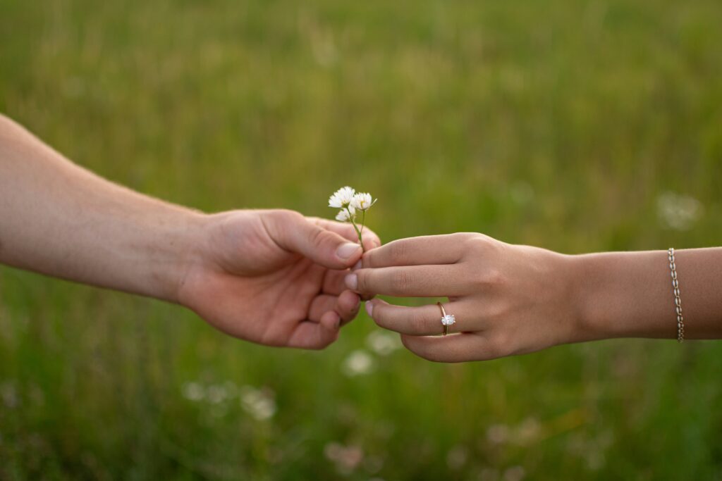 Man and woman holding a flower showcasing and engagement ring